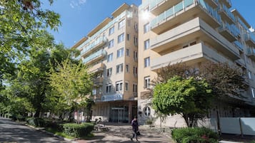 En flerplansbolig med altaner, en central indgang og grøn bevoksning omkring.