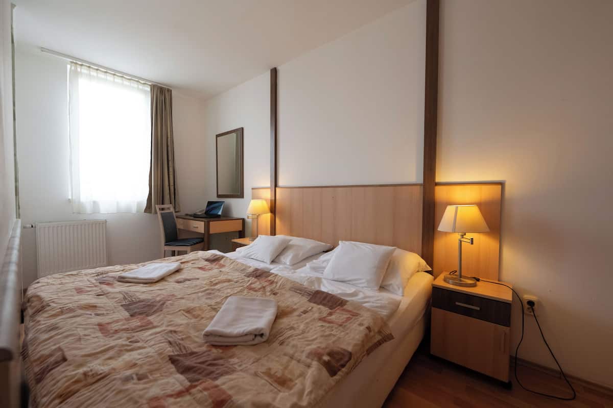 A hotel room with a bed, bedside tables, a desk, and a chair.