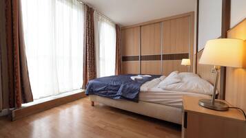 Une chambre d’hôtel avec un lit, une lampe de chevet, une armoire en bois et une fenêtre avec des rideaux.