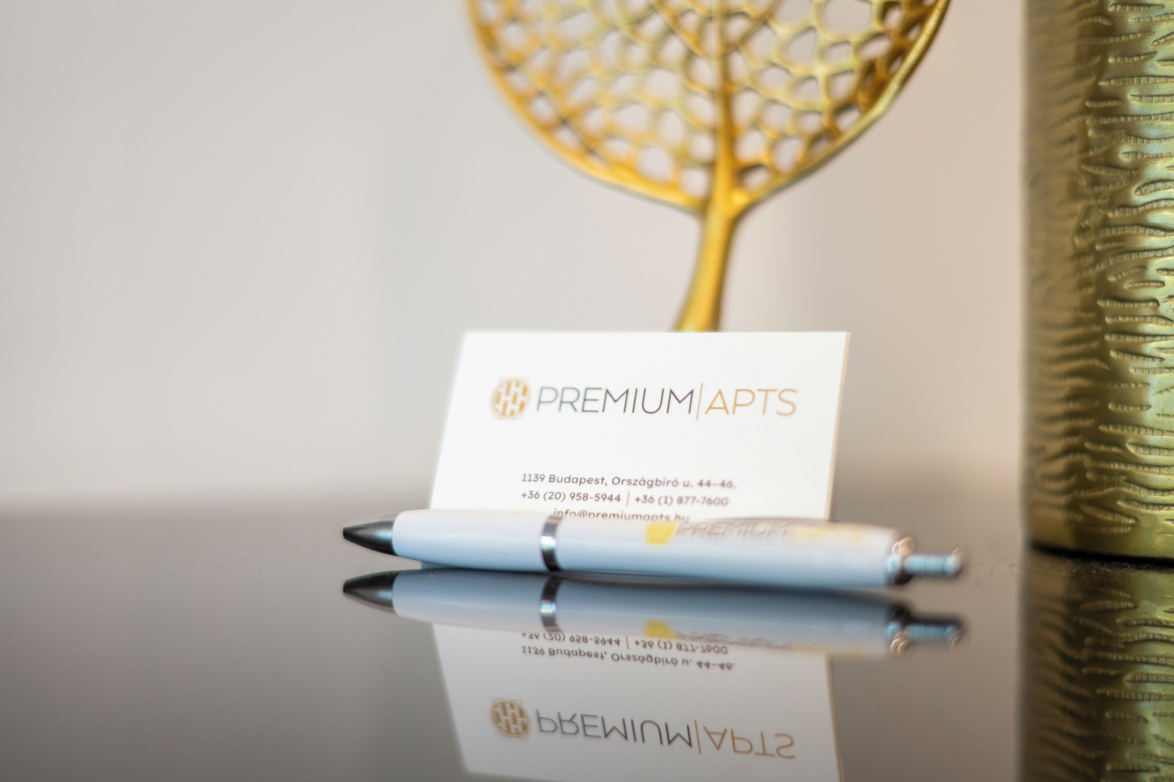Cartão de visita com 'PREMIUMAPTS' e informações de contato, colocado em uma superfície reflexiva com uma caneta ao lado.