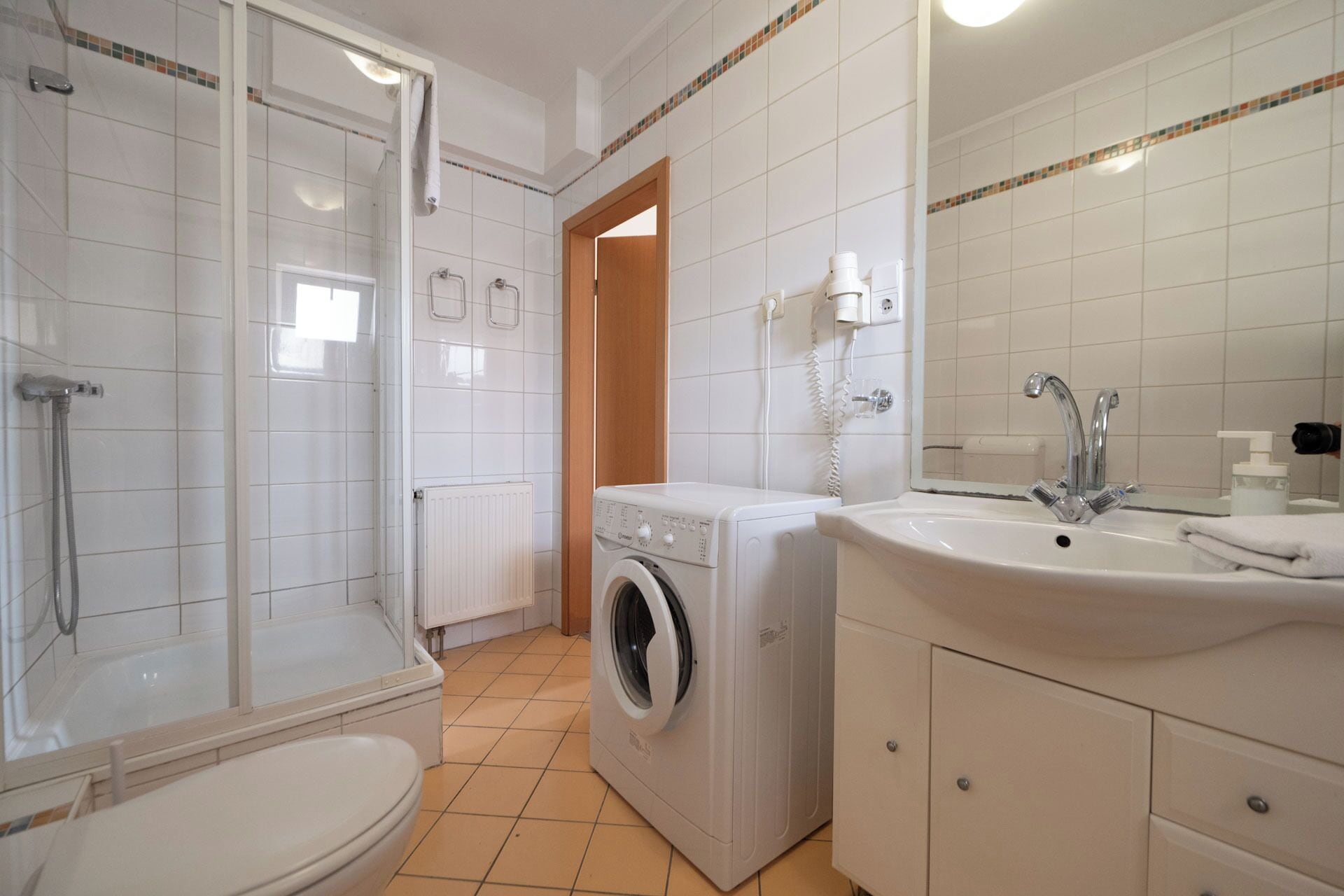 A bathroom with a shower, toilet, washing machine, and sink.