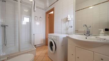 A bathroom with a shower, toilet, washing machine, and sink.