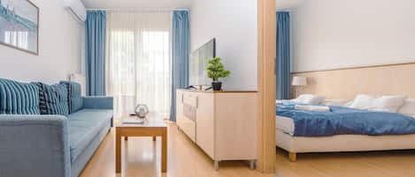 A modern hotel room with a sofa, a bed, a TV, a desk, and a potted plant.