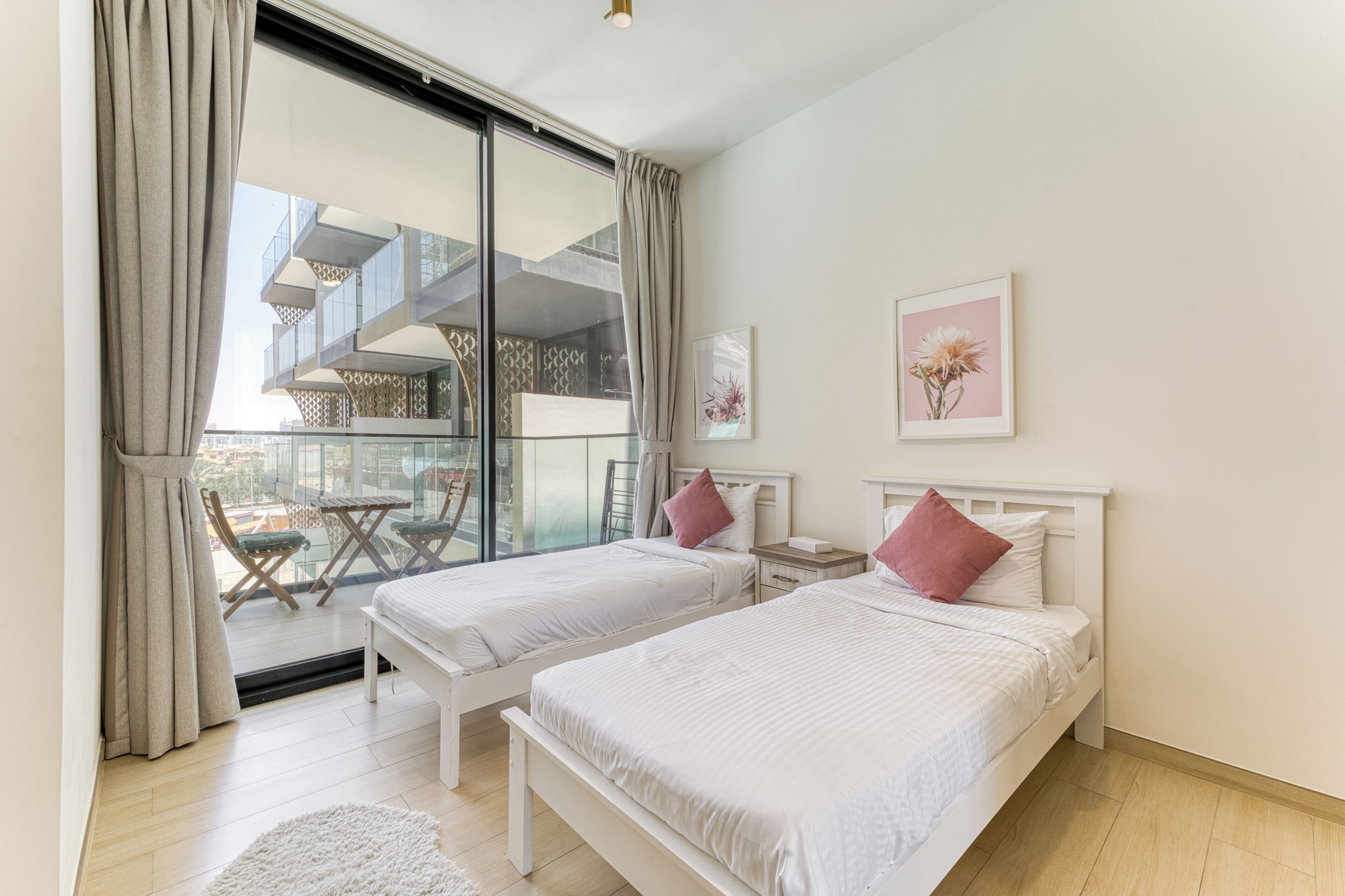 A bedroom with two beds, a balcony with a table and chairs, and a large window.