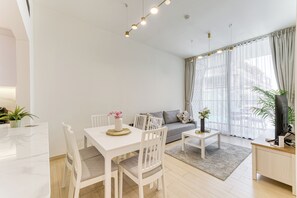 Ein modernes Wohnzimmer mit Essbereich, einer Couch, einem Fernseher und einem großen Fenster mit Vorhängen.