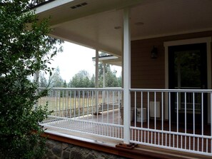 A covered porch with a railing, a stone foundation, and a view of a grassy yard. - Luxury Cabin Rental in the Cascade Mountains near Crater Lake, Southern Oregon (Prospect)