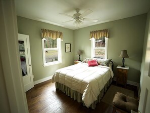 A bedroom with a bed, two windows with curtains, a ceiling fan, a nightstand, and a chair. - Luxury Cabin Rental in the Cascade Mountains near Crater Lake, Southern Oregon (Prospect)