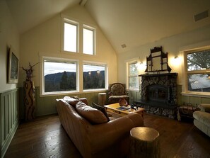 A cozy living room with a stone fireplace, a leather sofa, and a view of the outdoors through large windows.