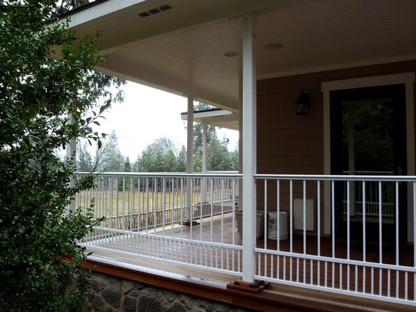 A covered porch with a railing, a stone foundation, and a view of a grassy yard.