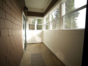 A narrow hallway with a brick wall, a white door, and a windowed alcove with a view of trees.