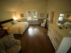 A bedroom with a bed, dresser, chair, and two windows.