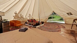 A tent with a bed, a chair, a small table, and a view of the outdoors. - Nature-Forward Glamping Resort with Forest Paths and Meadow Hangouts in Stanton, Kentucky (Stanton)
