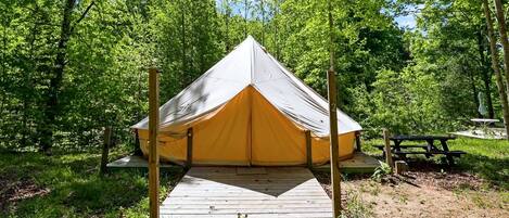 Une tente conçue pour une seule personne, dotée d’une terrasse en bois et située dans une zone boisée.