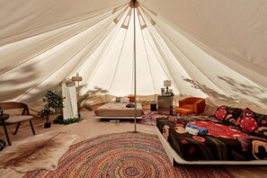 A tent with a bed, a chair, a small table, and a lamp.