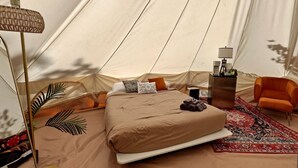 A tent-style room with a bed, a small table, a chair, and a lamp. - Nature-Forward Glamping Resort with Forest Paths and Meadow Hangouts in Stanton, Kentucky (Stanton)