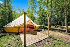 Ein Zelt mit einer Holzterrasse, einem Picknicktisch und bewaldeter Umgebung.