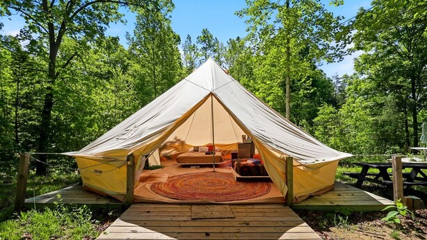 A tent with a wooden deck leading to it, surrounded by trees. - Nature-Forward Glamping Resort with Forest Paths and Meadow Hangouts in Stanton, Kentucky (Stanton)