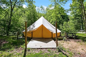 A single-occupancy tent with a wooden deck in a forested area.