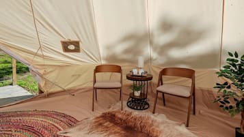 A tent with two wooden chairs, a small table with a candle, and a rug.