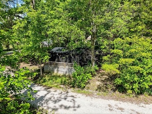 Un sentier de gravier mène à un pont en bois qui enjambe un petit bassin, le tout étant entouré d’un feuillage verdoyant et dense.
