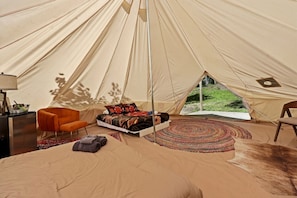 A tent with a bed, a chair, a small table, and a view of the outdoors.