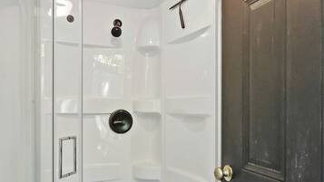 A shower with a glass door, a doorbell, and a door with a sign above it.