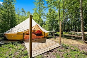 A tent with a wooden deck, a picnic table, and a forested background.