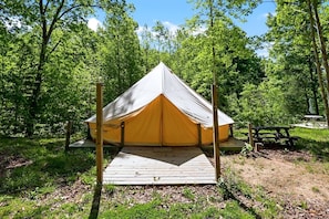 Ein Ein-Personen-Zelt mit einer Holzterrasse in einem bewaldeten Gebiet.