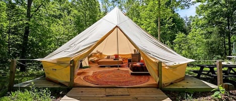 A tent with a wooden deck leading to it, surrounded by trees.
