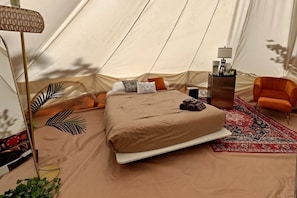 Habitación tipo tienda de campaña con cama, una mesita, una silla y una lámpara.