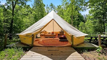 A tent with a wooden deck leading to it, surrounded by trees.