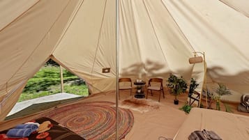 A tent interior with a dining area, chairs, a rug, and a table with a candle.