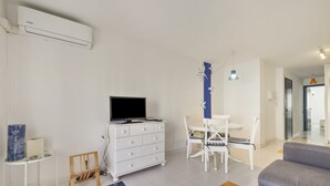 Una sala de estar moderna con televisor de pantalla plana, muebles blancos y una lámpara colgante azul.
