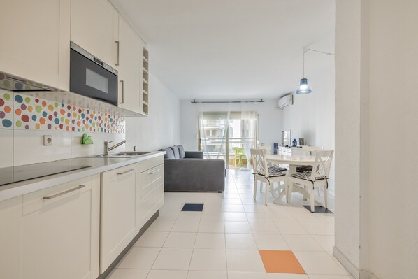 A modern kitchen with white cabinets, a microwave, and a colorful backsplash.