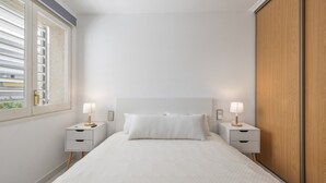 Un dormitorio con una cama, dos mesitas de noche con lámparas, una ventana y un armario de madera.