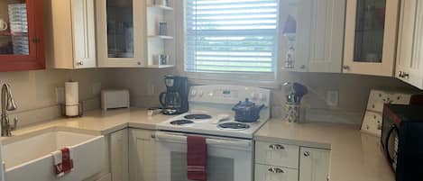 A kitchen with white cabinets, a stove, a sink, and a window with blinds.