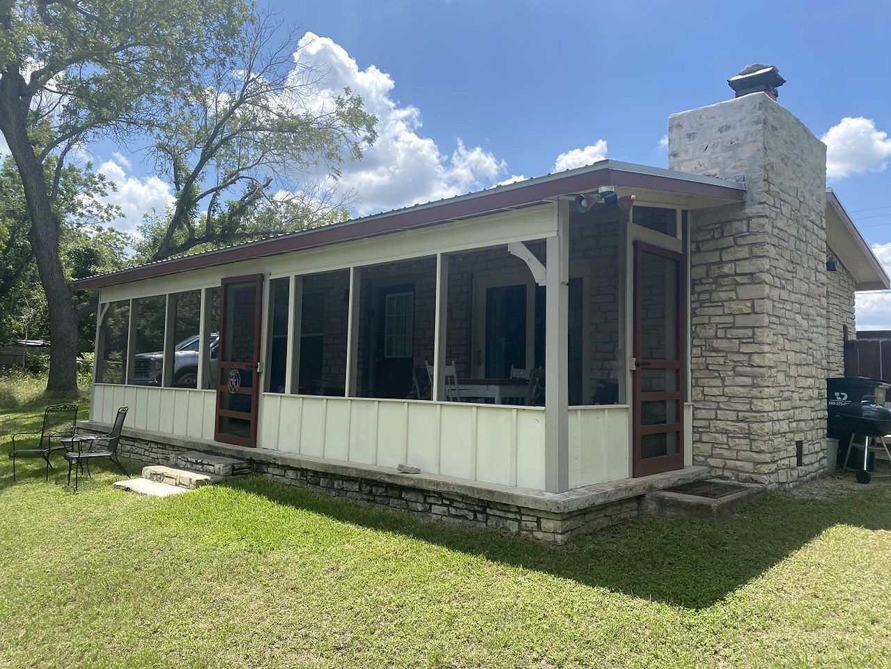 A single-story building with a stone chimney, a covered porch, and a carport.