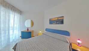 Ein Schlafzimmer mit Bett, Nachttisch, Lampe, Kommode, Spiegel und einem Bild an der Wand.