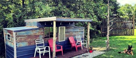 Eine kleine Holzhütte mit einer Veranda, zwei weißen Stühlen und zwei roten Stühlen.