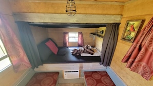 Um quarto pequeno e acolhedor com uma cama de solteiro, uma escada de madeira e uma mesinha.