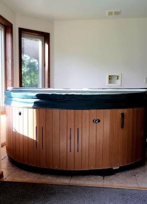 Ein Whirlpool in einem Raum mit Fenster, Tür und Temperaturregler an der Wand.
