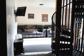 Ein Wohnzimmer mit einer Couch, einem an der Wand befestigten Fernseher und zwei gerahmten Bildern.