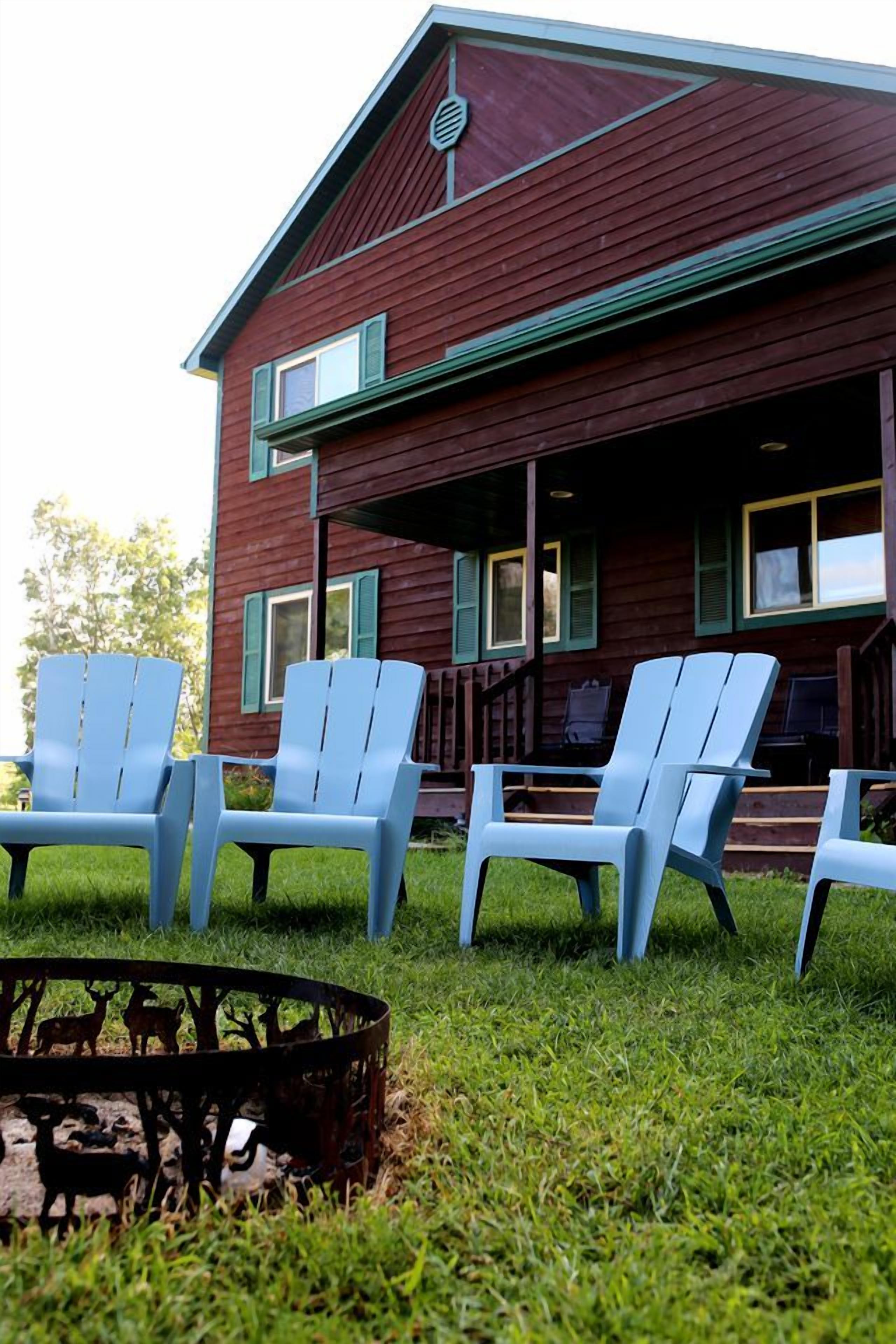 Een rood houten gebouw met een veranda en vier blauwe Adirondack-stoelen.