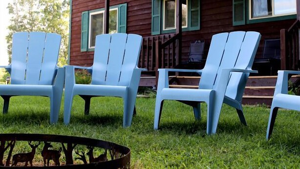 A red wooden building with a porch and four blue Adirondack chairs.
