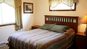 A bedroom with a bed, nightstands, a lamp, a window with curtains, and a framed picture on the wall.
