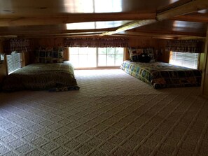 A cabin bedroom with two beds, a large window, and a wooden ceiling.