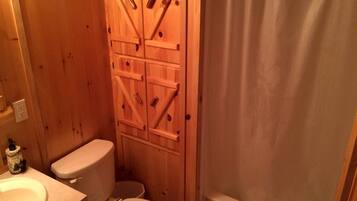 A small bathroom with a wooden door, a toilet, a sink, and a shower curtain.