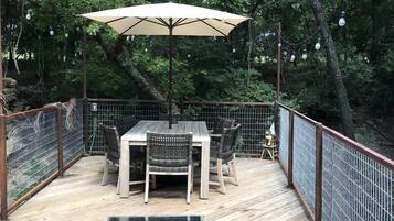 A wooden deck with a table and chairs, surrounded by a metal fence, set in a wooded area.