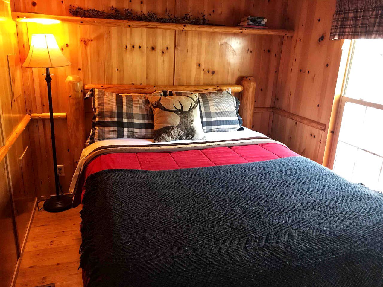 Una habitación tipo cabaña de madera con una cama, una lámpara y una ventana.