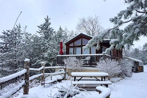 En stuga med en träveranda, omgiven av snötäckta träd.